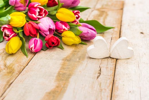 Colorful bunch of tulips and two white hearts on rustic wooden table with copy space