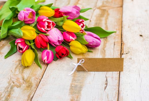 Beautiful tulips bouquet with empty tag on wooden table background