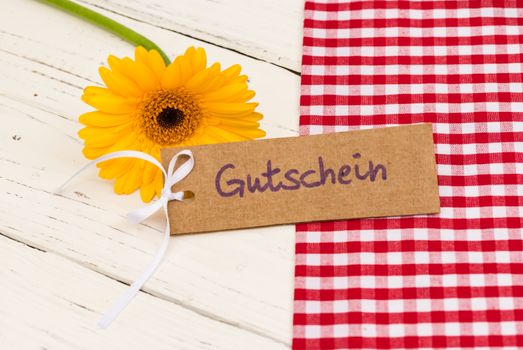 Yellow gerbera daisy flower with gift card with german word, Gutschein, means voucher or coupon