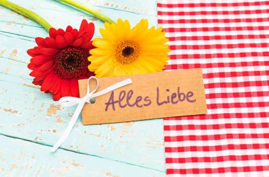 Red and yellow gerbera flowers with card with text, Alles Liebe, means love