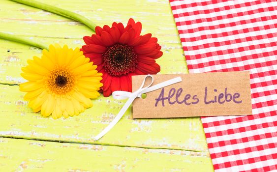 Red and yellow gerbera flowers with card with german text, Alles Liebe, means love