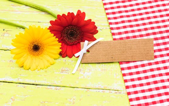 Red and yellow gerbera flowers on wooden table with blank label for a message
