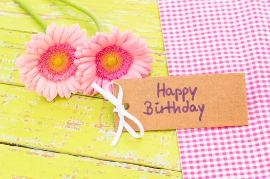 Beautiful pink gerbera flowers with Happy Birthday greeting card on wooden table background