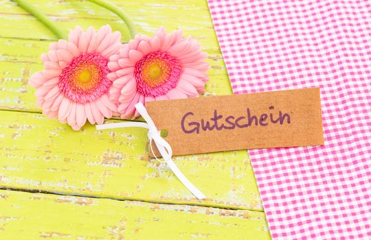 Beautiful pink gerbera flowers with card with german word, Gutschein, means voucher or coupon