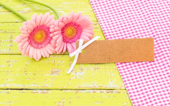 Pink gerbera daisy flowers with empty label on wooden table background