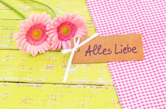 Pink gerbera flowers with card with german text, Alles Liebe, means love