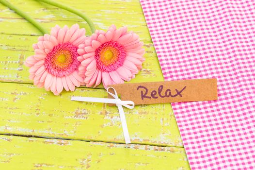 Pastel pink flowers with gift card with the word relax decorated on colored wooden table