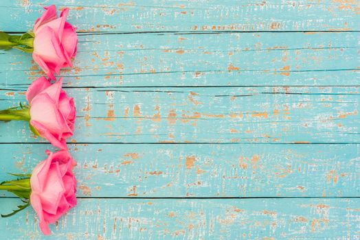 Romantic pink rose flowers side border on pastel blue wooden background with copy space