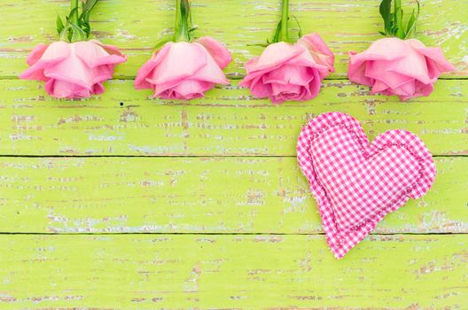 Pink roses with romantic heart on green wooden background with copy space