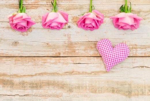 Romantic flowers arrangement with pink roses and fabric heart on vintage wood