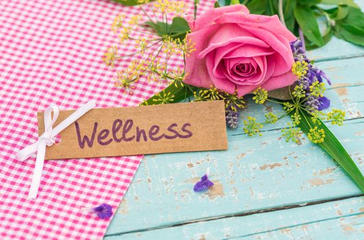 Bouquet of flowers and card with the word wellness on wooden background