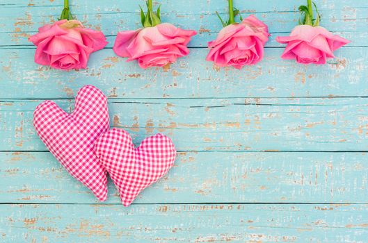 Love background with two hearts and pink rose flowers on light blue wood with copy space