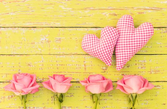 Pink roses flower arrangement with two hearts on yellow wooden background with copy space