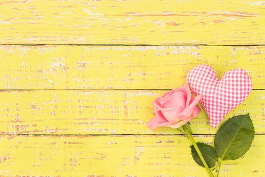 Romantic love background with pink heart and rose flower on yellow rustic wood with copy space