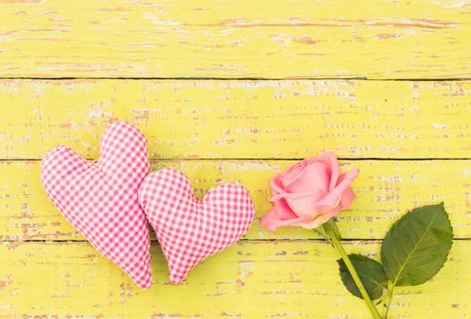 Pink rose flower with two hearts on rustic yellow wooden background with copy space
