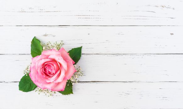 Pink rose blossom with gypsophila on white wooden table, top view with copy space
