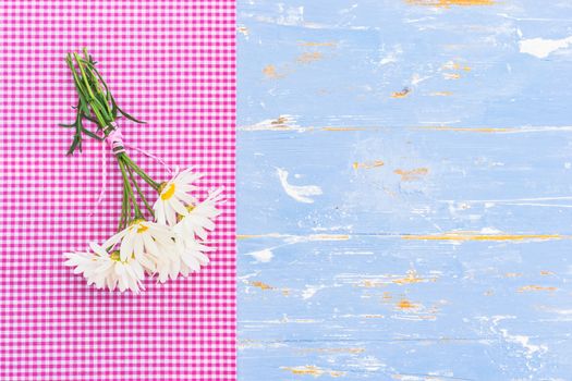 Beautiful bouquet of daisy chamomile flowers with pink border on blue wood with copy space