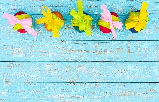 Multicolored easter eggs with ribbon bow on blue wooden background