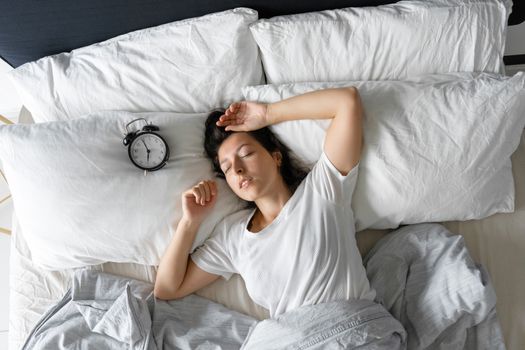 Top view of a girl sleeping next to an alarm clock. Time to wake up. On the wake-up clock 7 a.m. Deep sleep