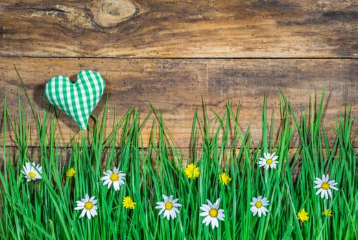 Wooden background with beautiful fresh green meadow with flowers and green heart