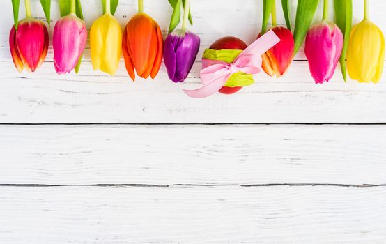 Easter background with multicolored tulips and easter egg on white wood with copy space