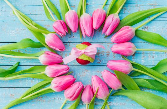 Pink easter egg ornated with ribbon bow and framed of beautiful  tulips on blue wood