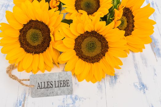 Bouquet of yellow sunflowers and greeting card with german text, Alles Liebe, means best wishes