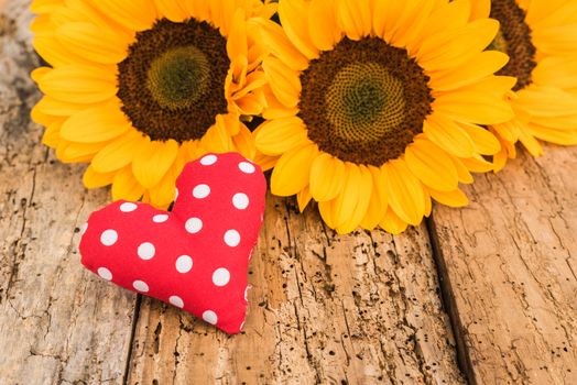 Romantic red heart with yellow sunflowers on rustic wooden background