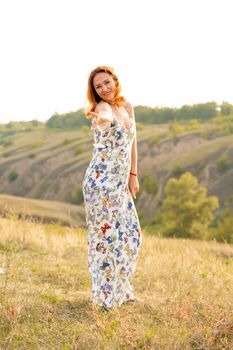 Beautiful red-haired girl is having fun and dancing in a field at sunset.