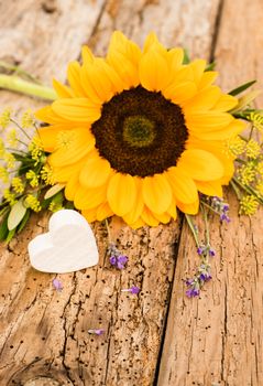 Bunch of flowers with yellow sunflower and little heart on rustic wooden background