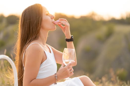 Gorgeous young brunette girl in a white sundress enjoying a picnic in a picturesque place. Romantic picnic.