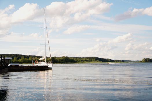 Yacht on blue peaceful lake on green forest and blue sky background in sunny day