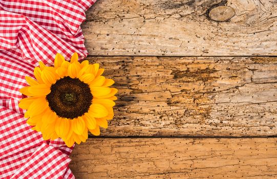 Red checked table cloth with yellow flower on old rustic wood background and copy space