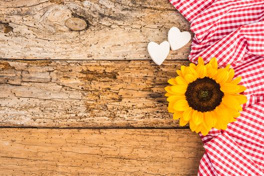 Yellow sunflower and two hearts with red fabric on rustic wooden background