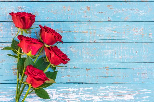 Bunch of red roses on blue wooden background with copy space