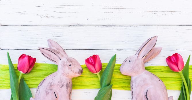 Easter bunnies and tulip flowers border on white wooden background with copy space
