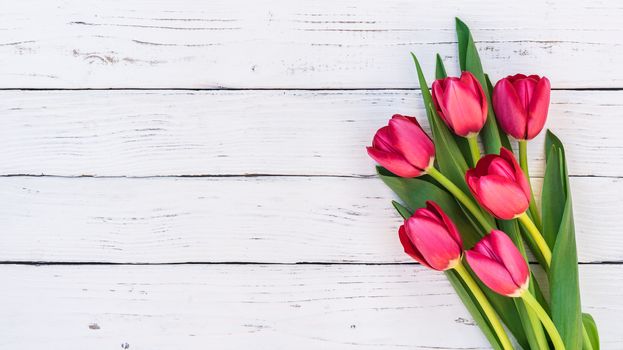 Red tulip spring flowers arrangement on white wooden table with copy space