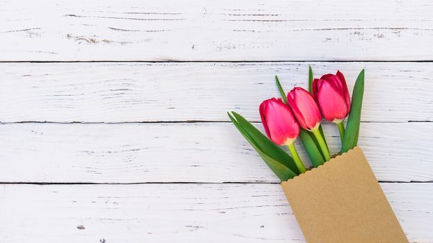 Red tulip flowers in paper bag on white wooden background with copy space
