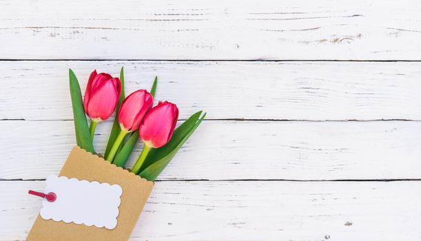 Bouquet of red tulip spring flowers with empty label on white wooden background