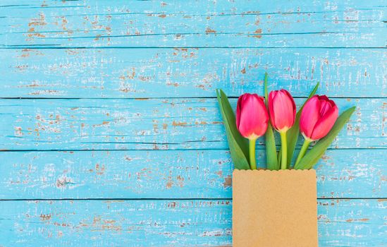 Red tulips arrangement in paper bag on blue wooden background