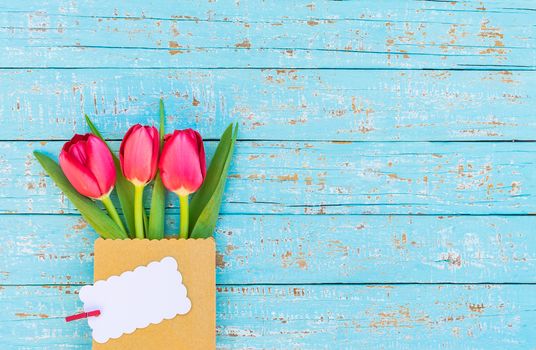 Red tulip spring flowers bunch with empty label on blue wooden background