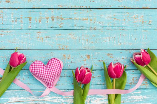 Romantic frame of pink heart with tulips on blue wooden background with copy space