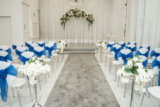 Bright room for weddings. Rows of guest chairs decorated with blue cloth.