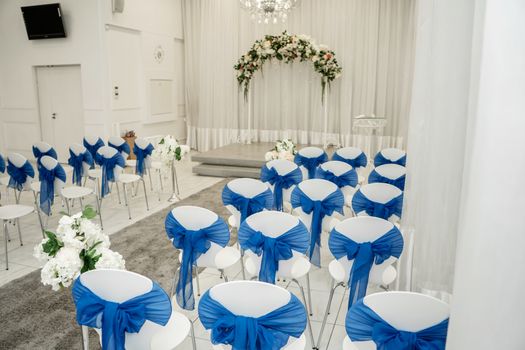 Bright room for weddings. Rows of guest chairs decorated with blue cloth.