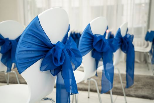 Bright room for weddings. Rows of guest chairs decorated with blue cloth.