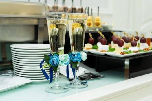 Champagne glasses are decorated with a blue ribbon with a flower. Festive banquet table for a wedding celebration