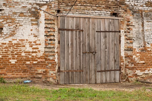 Old cowshed. Large wooden gate and dried wood. Old brick building.