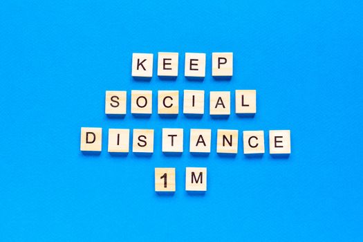 Words keep social distance 1 m. Wooden inscription on a blue background. Information sign of keep social distance 1 m from blocks. flat layout