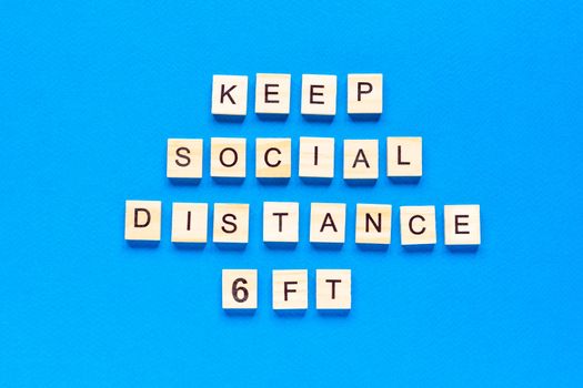 Words keep social distance 6 ft. Wooden inscription on a blue background. Information sign of keep social distance 6 ft from blocks. top view