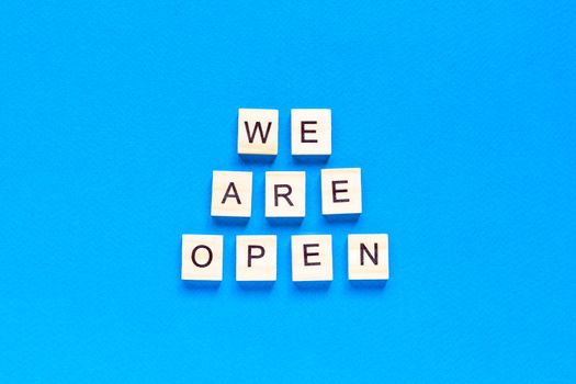 We are open. Wooden cubes with a text message We are open on a blue background. The view from the top. Flat layout. An office, cafe, or store welcomes guests after a coronavirus outbreak. The end of quarantine.